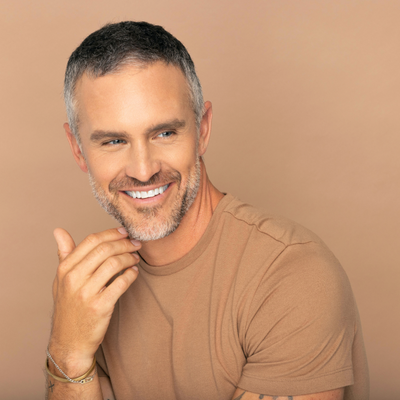 smiling man in tan t-shirt with his hand on his chin