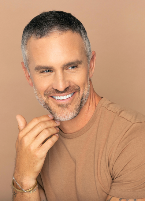 smiling man in tan t-shirt with his hand on his chin